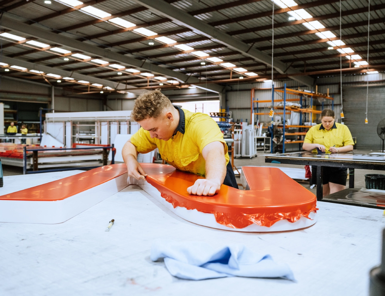Factory workers assembling large orange sign.
