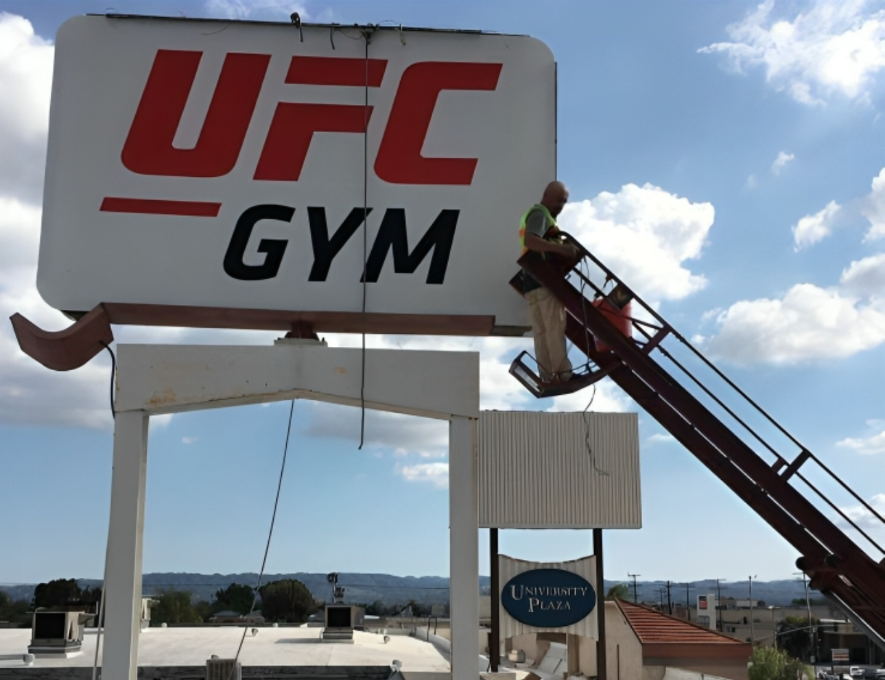Worker on ladder near UFC Gym sign.