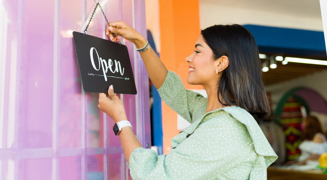 Woman hanging an "Open" sign on door.