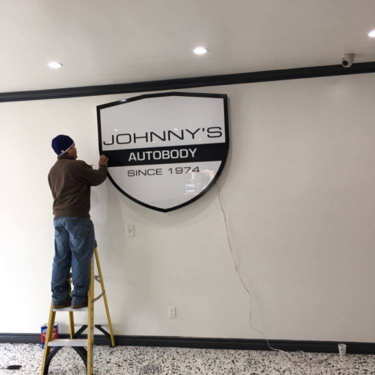 Person installing Johnny's Autobody sign indoors.