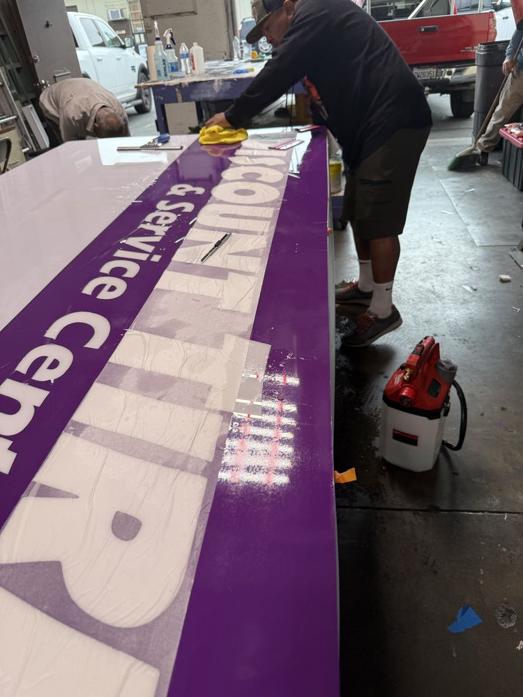 Man cleaning large purple sign in workshop.
