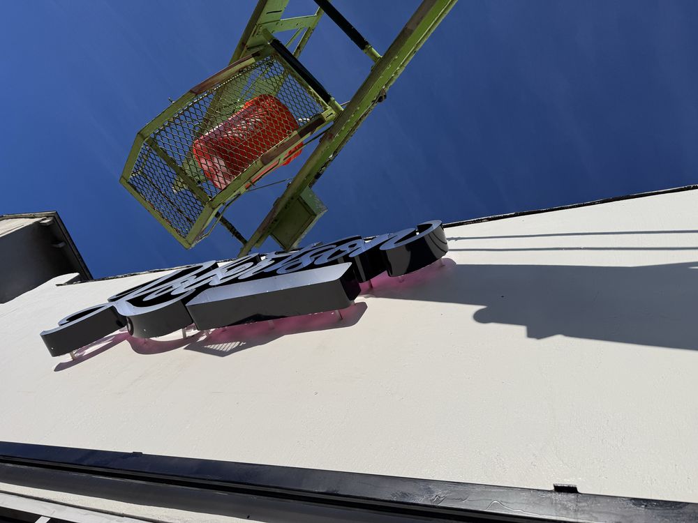 Sign installation with crane against blue sky.
