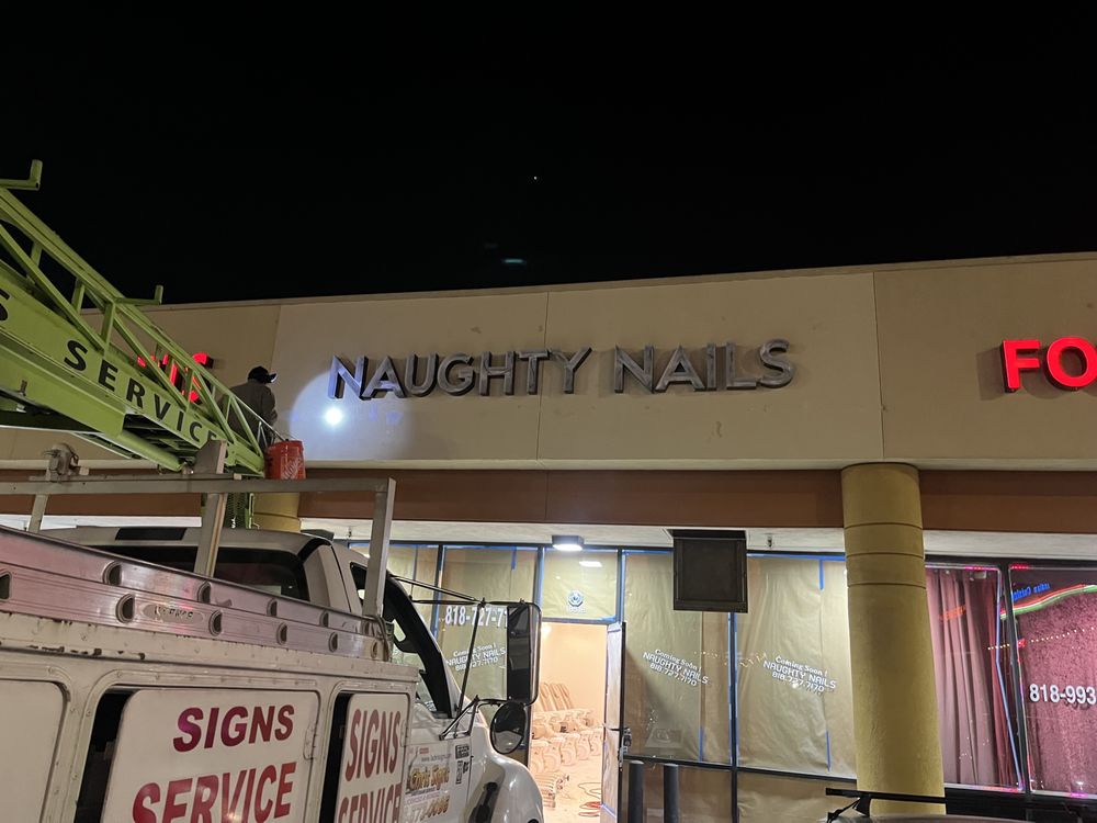 Sign installation for "Naughty Nails" at night.