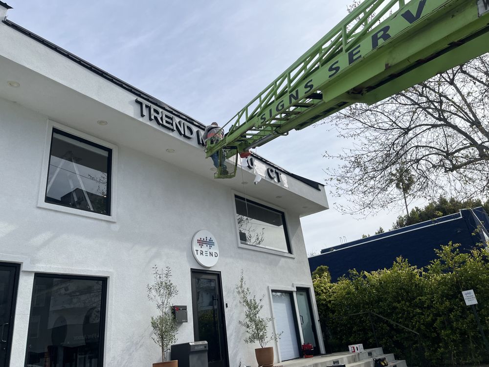 Worker on lift near building sign installation.