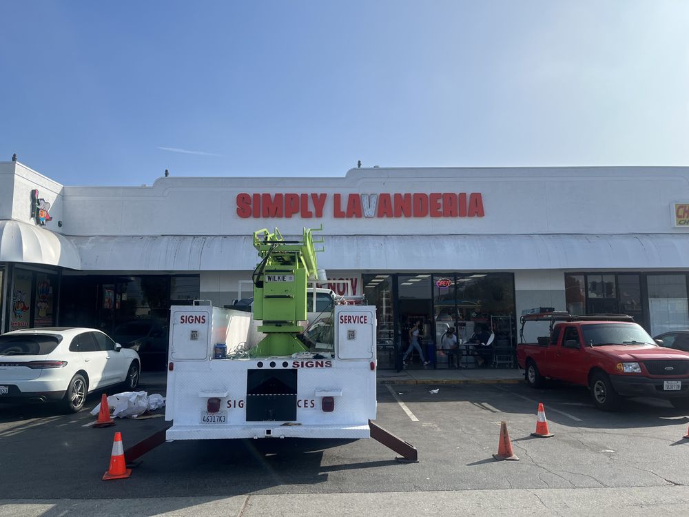 Sign installation at laundromat with vehicles parked.