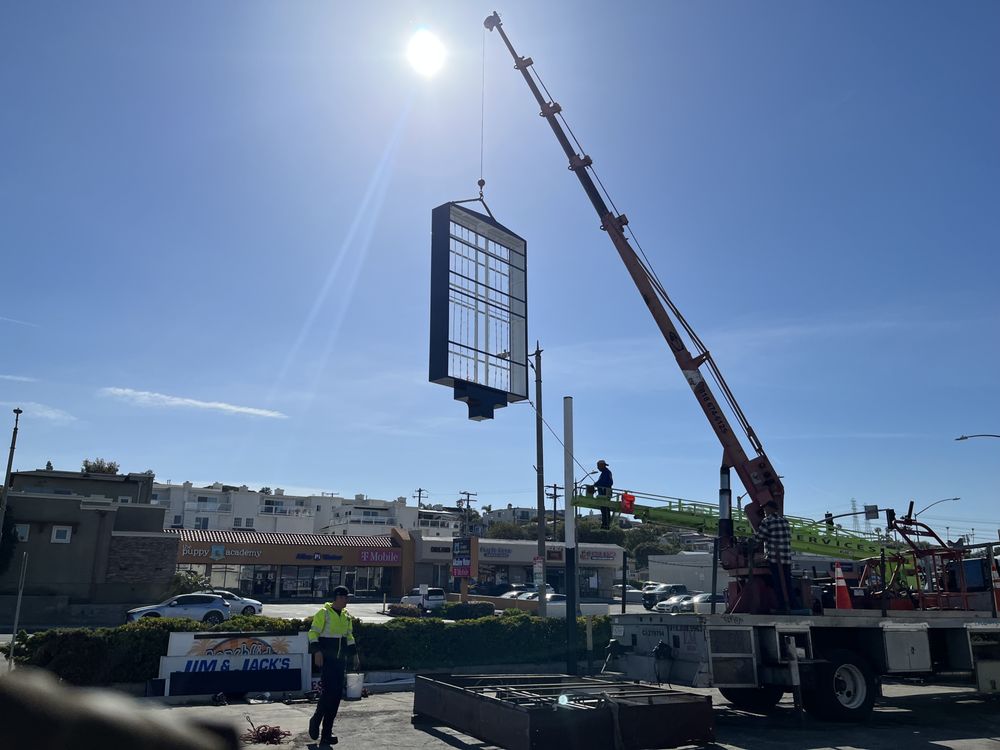 Crane lifting large sign in sunny sky.