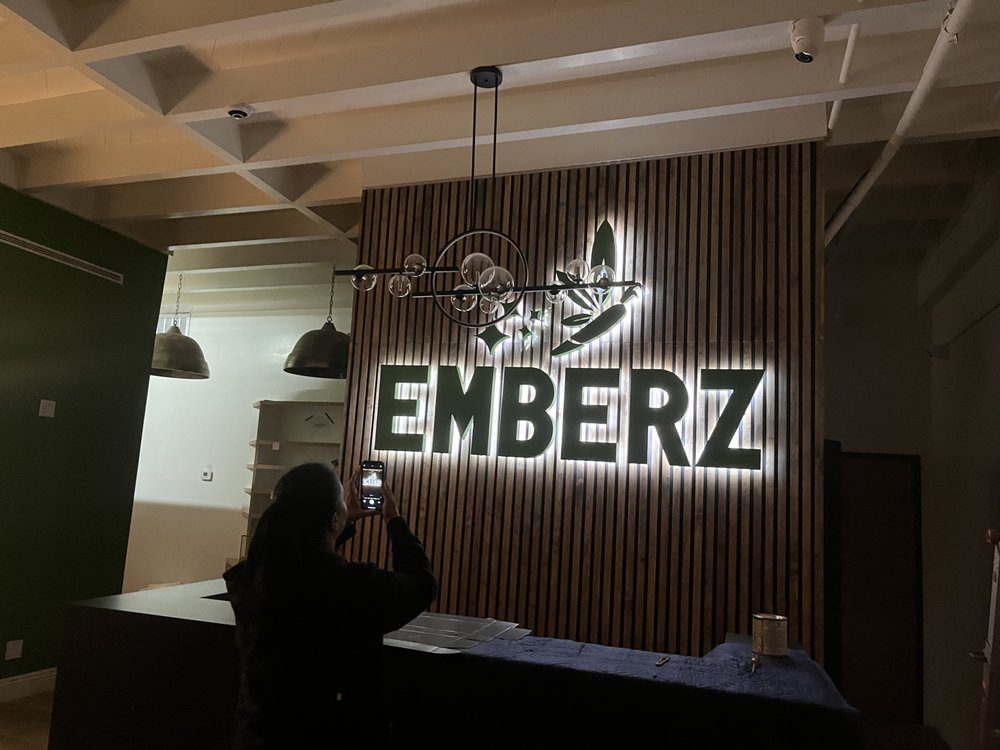 Person photographing illuminated "EMBERZ" sign indoors.