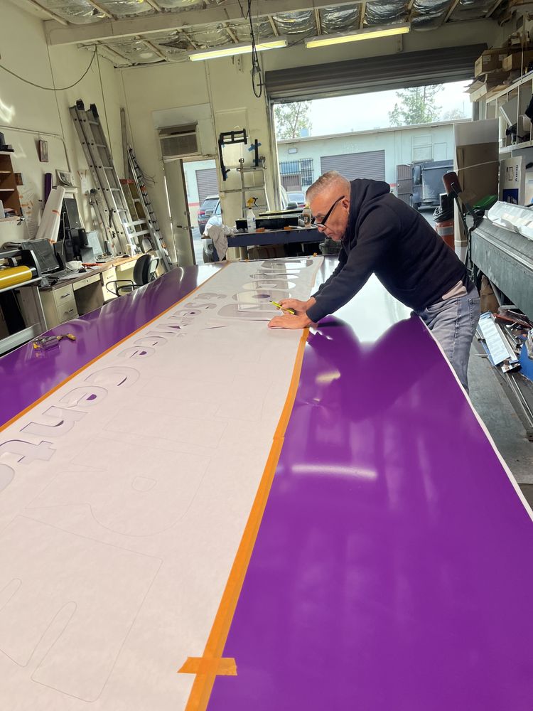 Man working on large purple sign indoors.