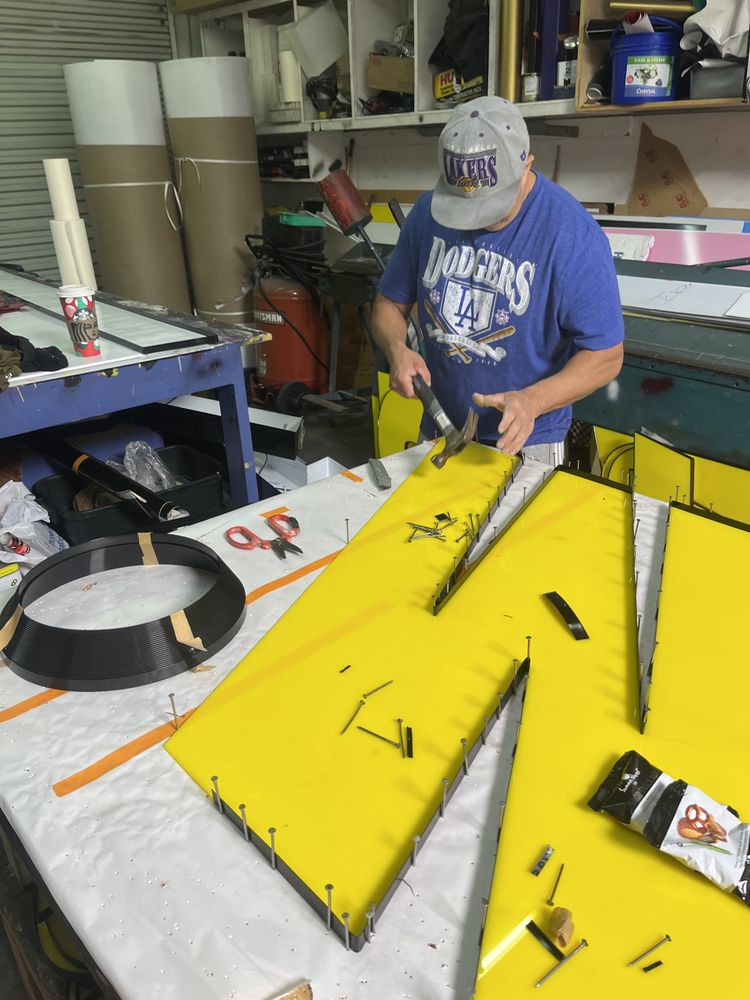 Man working on large yellow sign indoors.