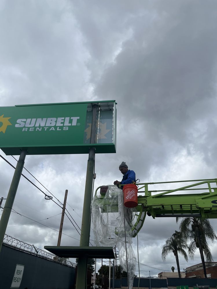 Worker maintaining Sunbelt Rentals sign in lift.
