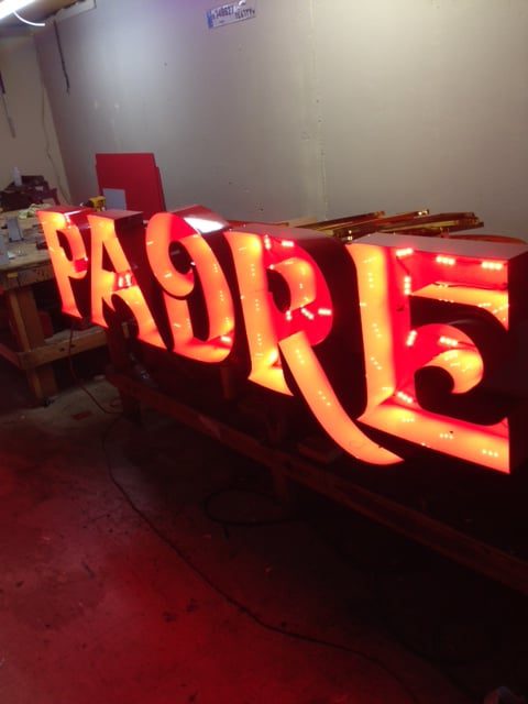 Illuminated "PADRE" sign in workshop.