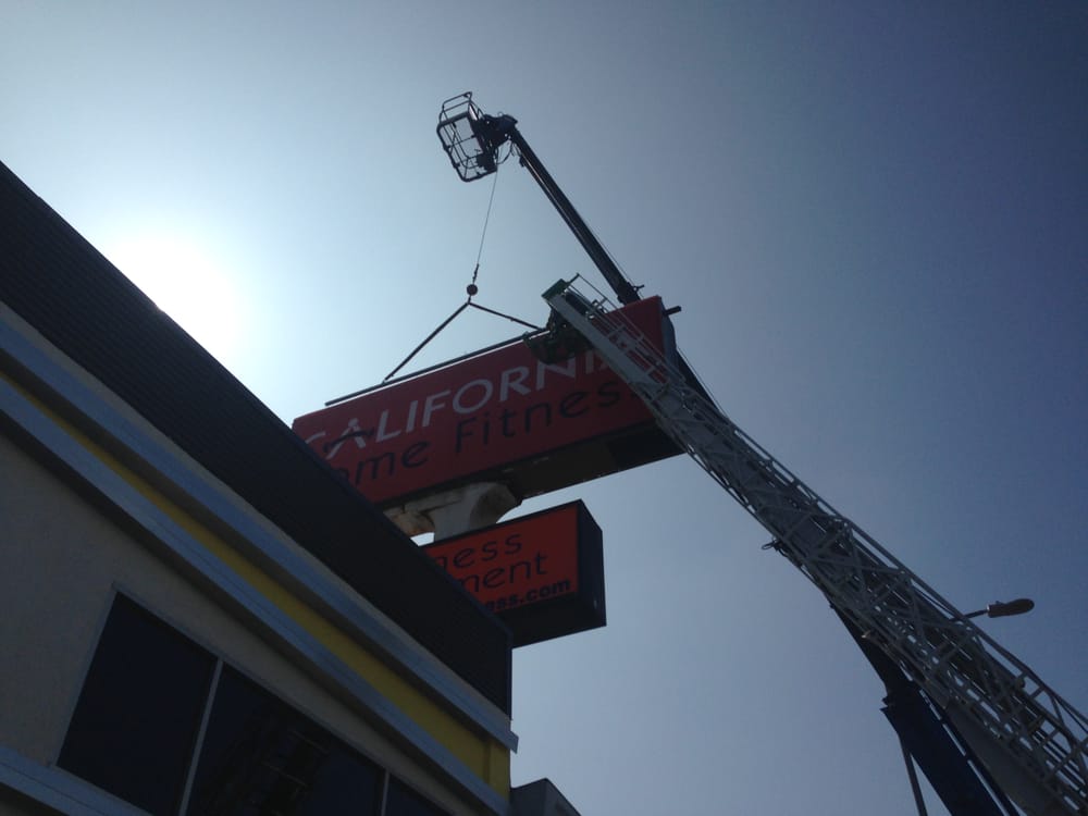 Crane lifting gym sign in sunlight.