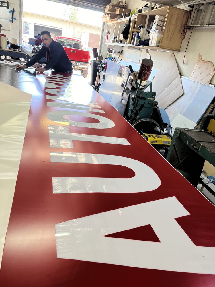 Man working on large red sign in workshop.