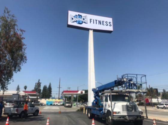 Crane truck near Crunch Fitness sign installation.