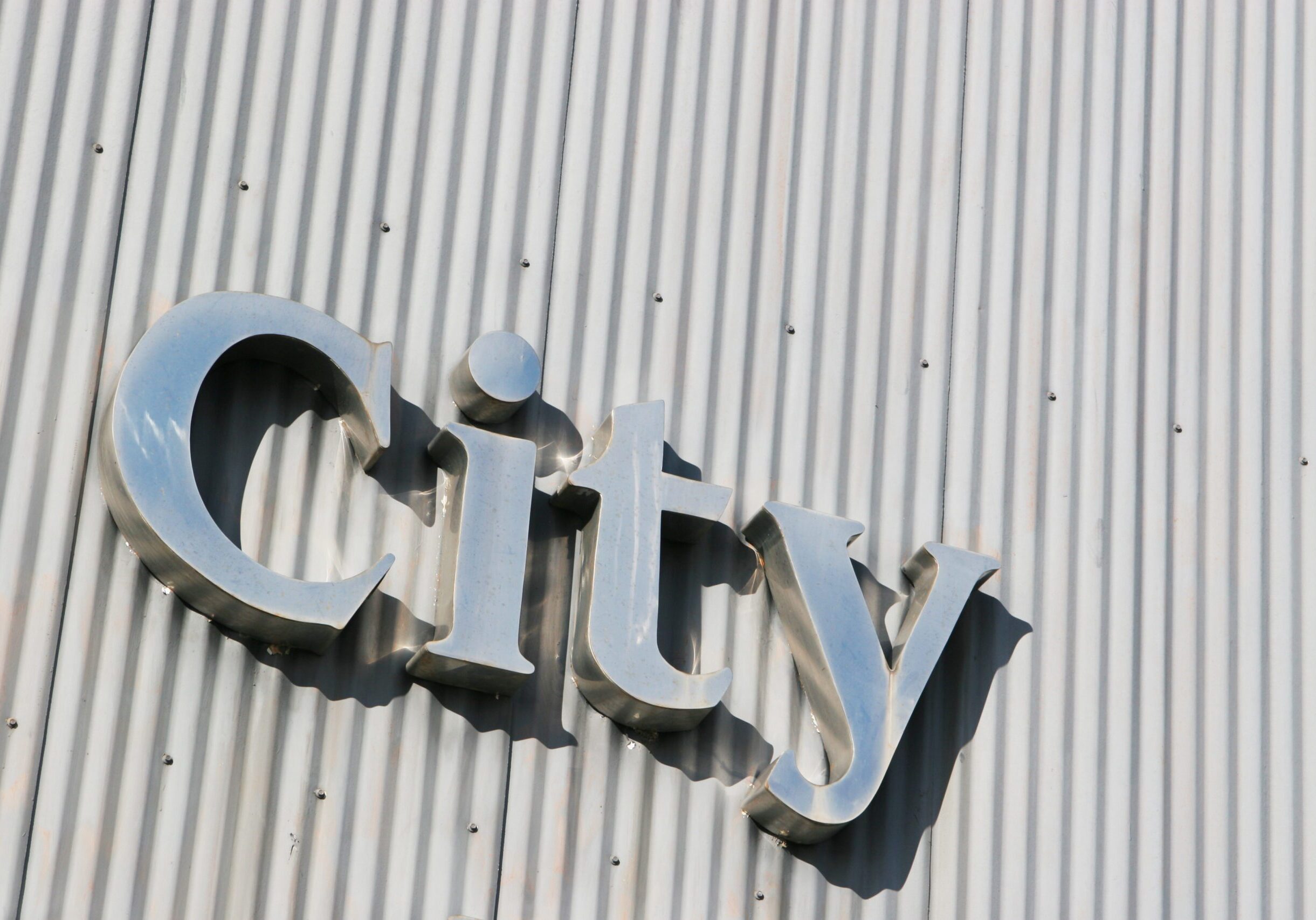 Metallic 'City' sign on corrugated wall.